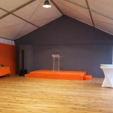 Salle avec une scène, un pupitre transparent et des éléments orange sur les murs.