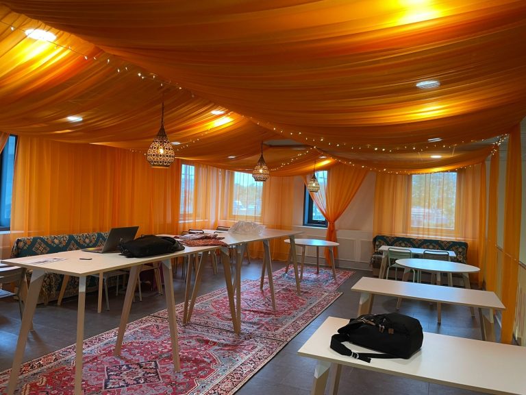 Salle de réunion décorée de drapés oranges et tables blanches sur un tapis rouge.