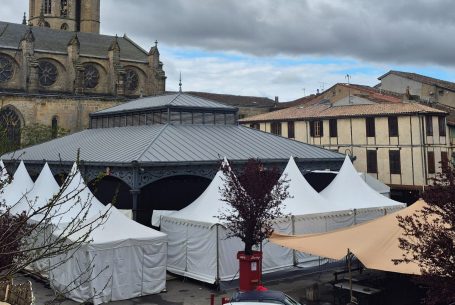 Tentes blanches installées sur une place avec un bâtiment historique en arrière-plan.