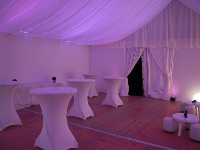 Intérieur d'une tente avec tables rondes blanches et éclairage violet.