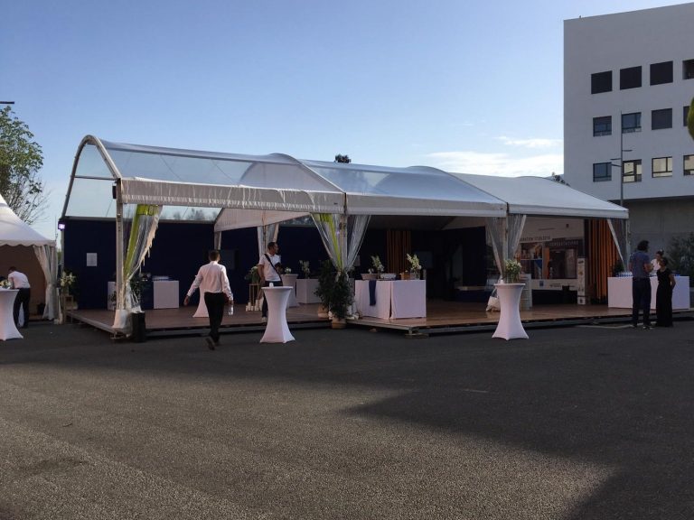 Tente de réception en plein air avec des tables et des invités, sous un ciel dégagé.